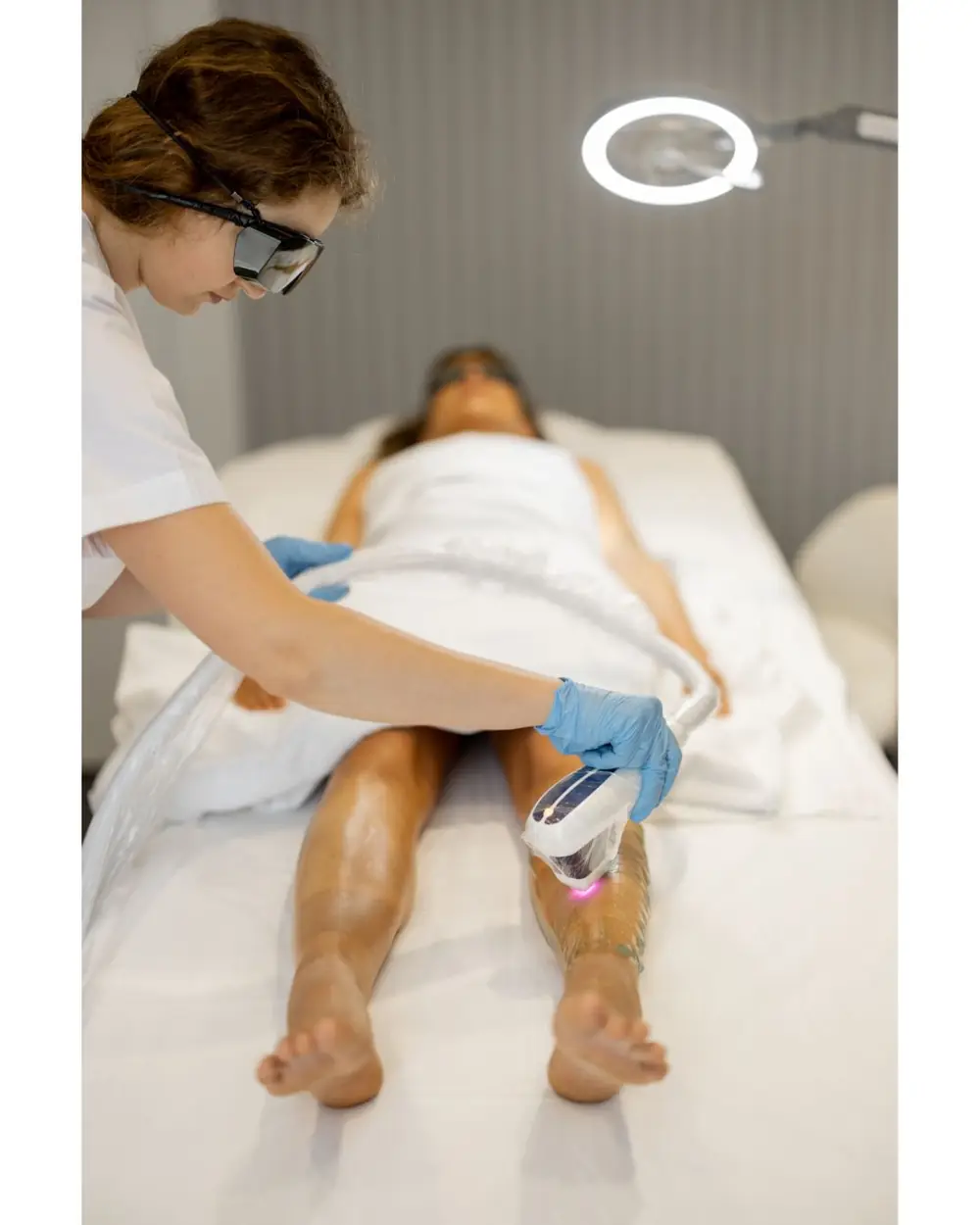 Practitioner wearing protective goggles and blue gloves performing a laser treatment on a client